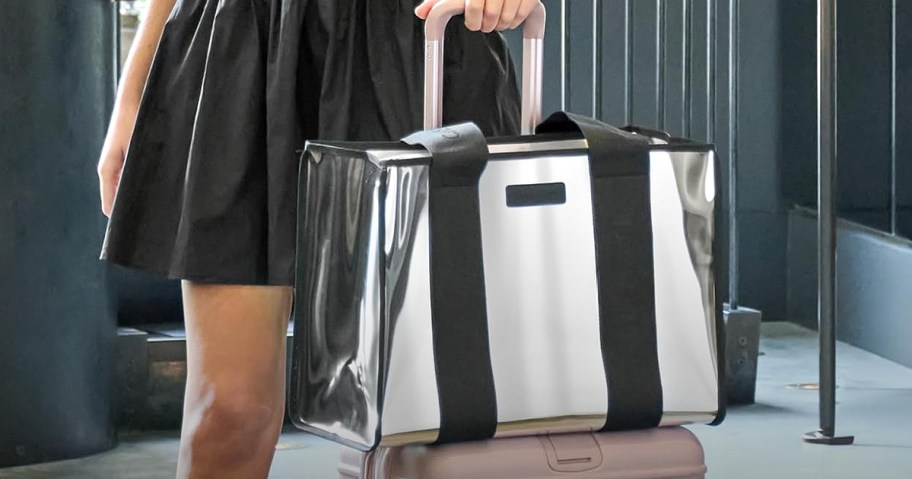 A metallic silver tote bag with black straps resting on top of a pink suitcase.