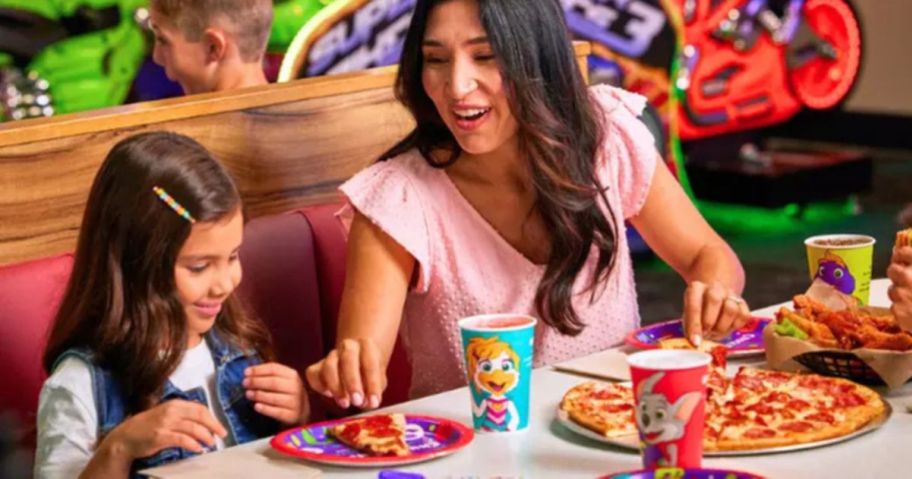 a woman and child sitting at a table with pizza and drinks
