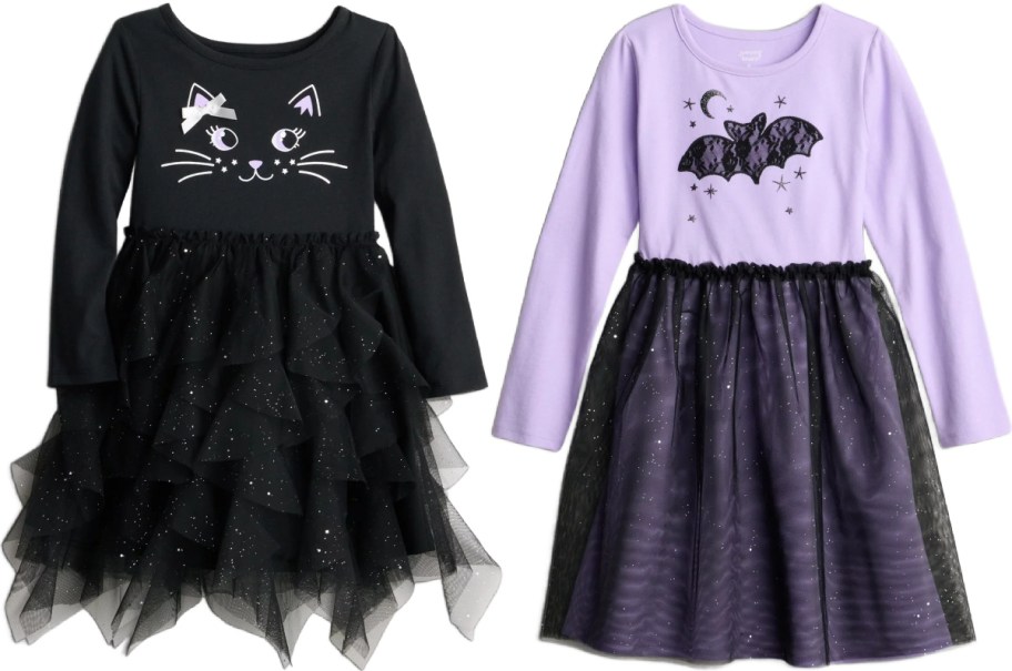 Two Jumping Beans kids' Halloween dresses shown side by side, featuring a black long-sleeve dress with a cat face graphic and a tiered sparkly tulle skirt on the left and a light purple long-sleeve dress with a lace bat and moon graphic and a sparkly black tulle skirt on the right.