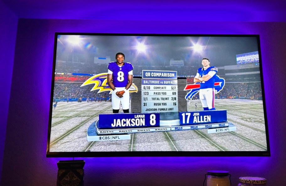 purple lights behind tv with ravens and bills quarterbacks on screen