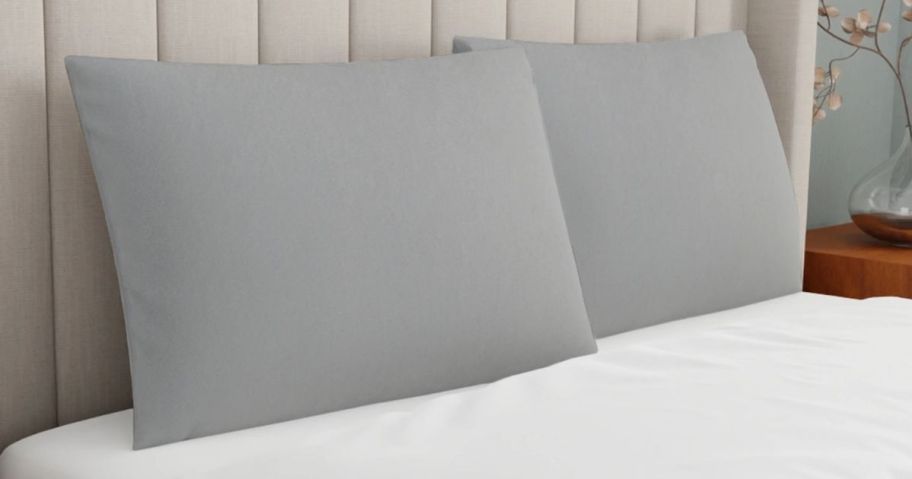 two bed pillows with silver cases on them on bed