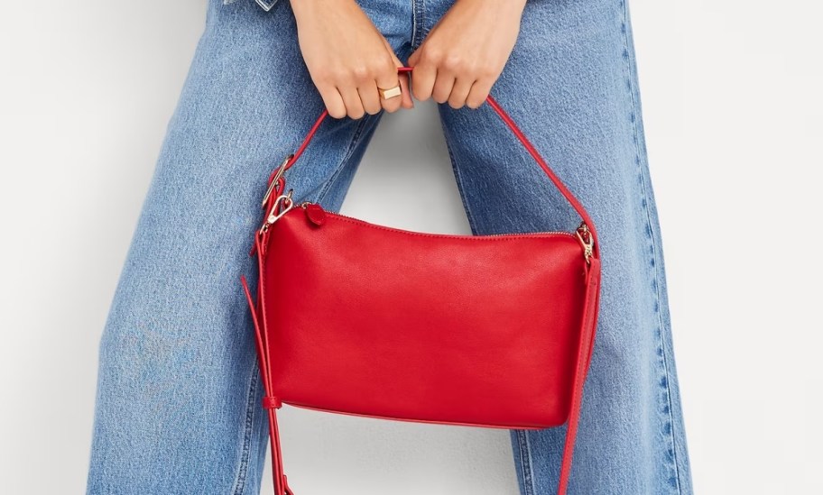 a woman in a pair of jeans holding a red shoulder bag