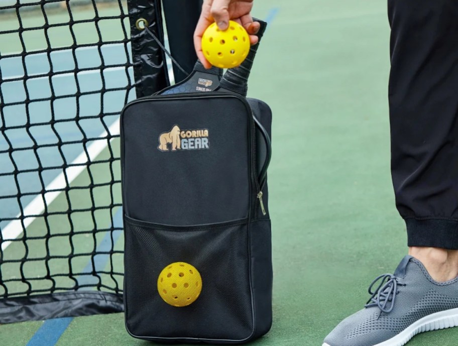 hand holding pickleball on court with bag of paddles