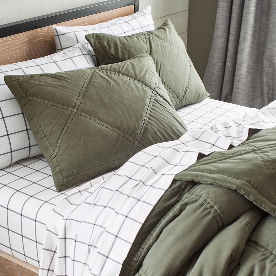white plaid sheets on bed with green shams and quilt