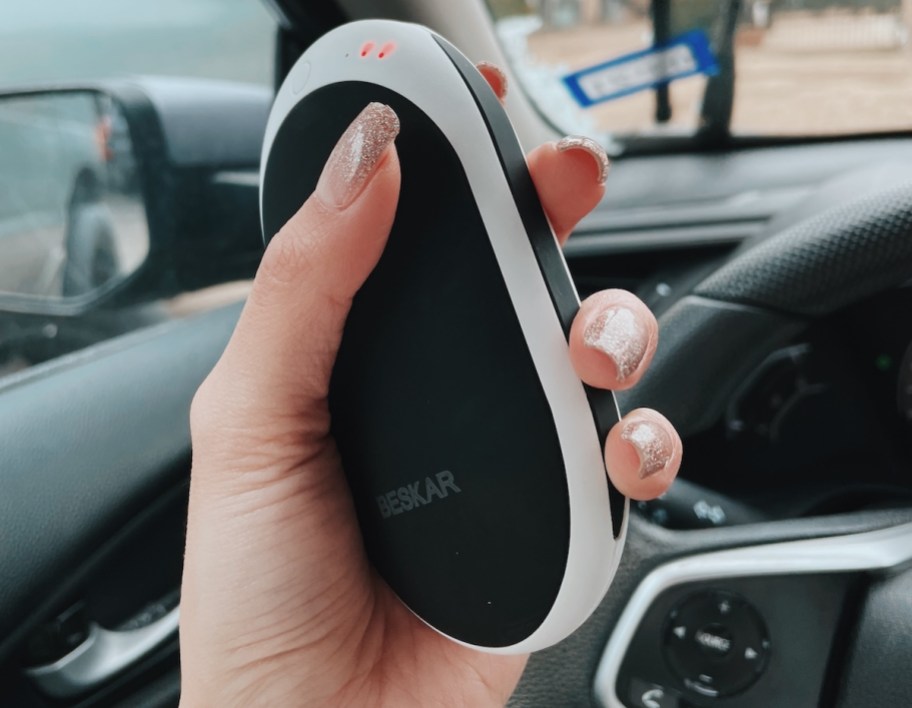hand holding a rechargeable hand warmer in car