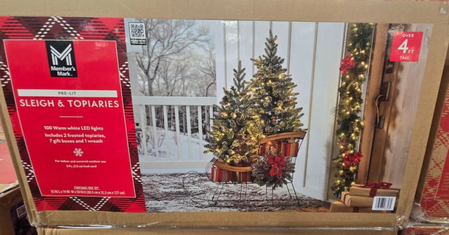 a box with prelit Christmas trees in a wooden sleigh