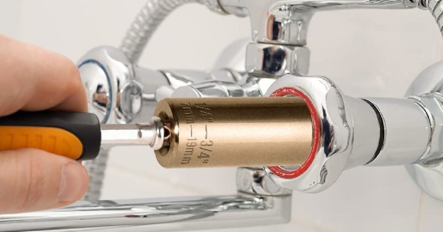 A person uses a wrench to tighten a shiny silver faucet in a bathroom. The tool is fitted onto a nut.