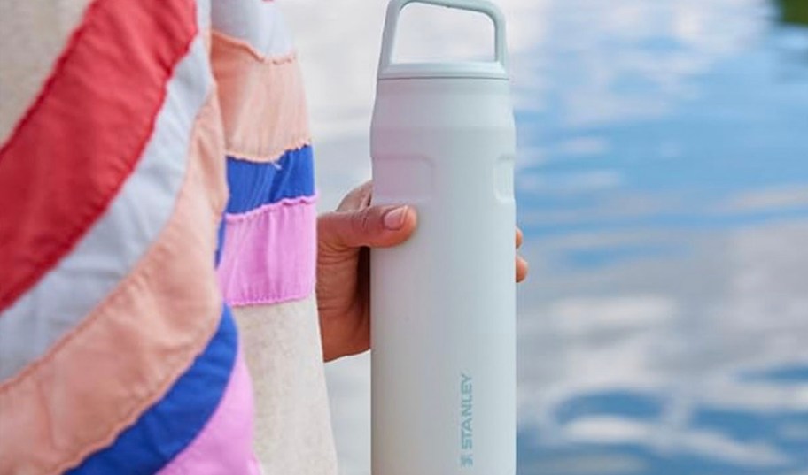 person holding white stanley tumbler near lake