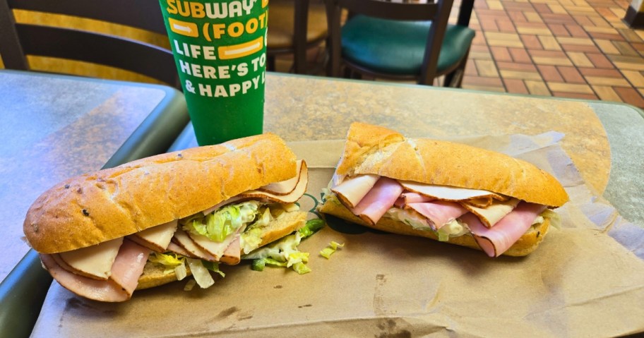a Subway foot long sub cut in half on a table next to a drink