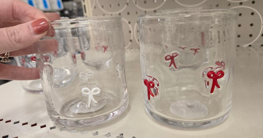 hand reaching for a juice glass with white bows, one with red bows sits beside it on a store shelf