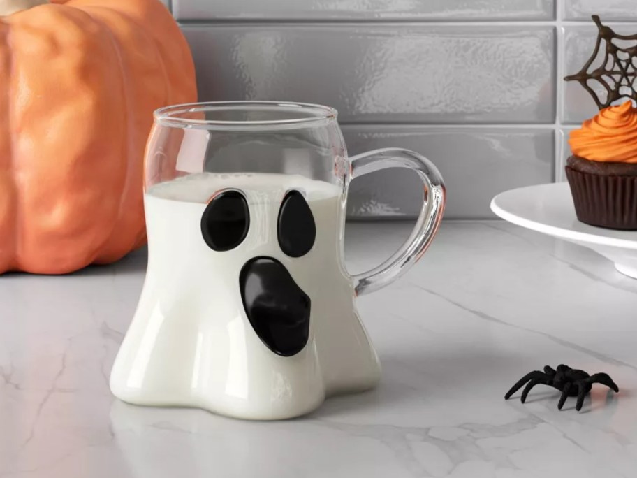 a glass ghost shaped mug filled partly with milk on a kitchen counter