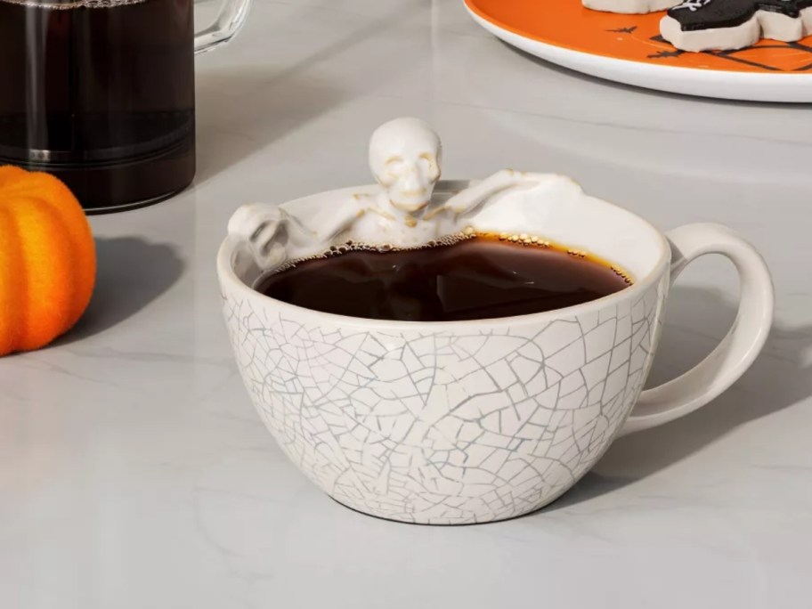 a coffee mug with a cracked pattern and a skeleton sitting inside on a kitchen counter