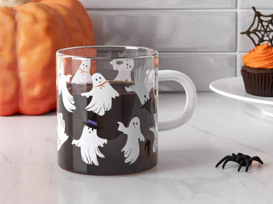 a glass coffee mug with ghosts and witches hats filled partly with coffee on a kitchen counter