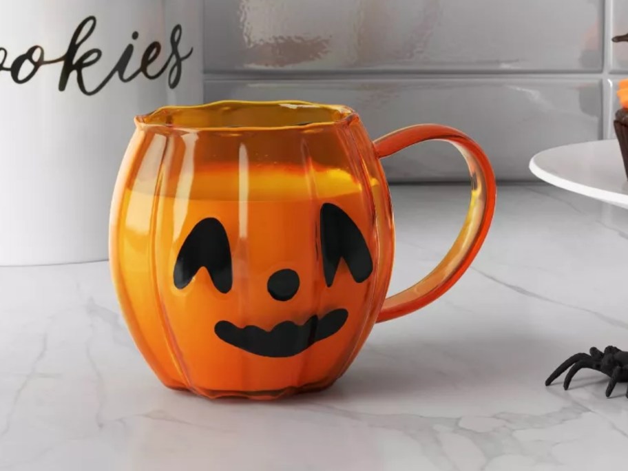 an orange glass pumpkin shaped jack-o-lantern mug on a kitchen counter