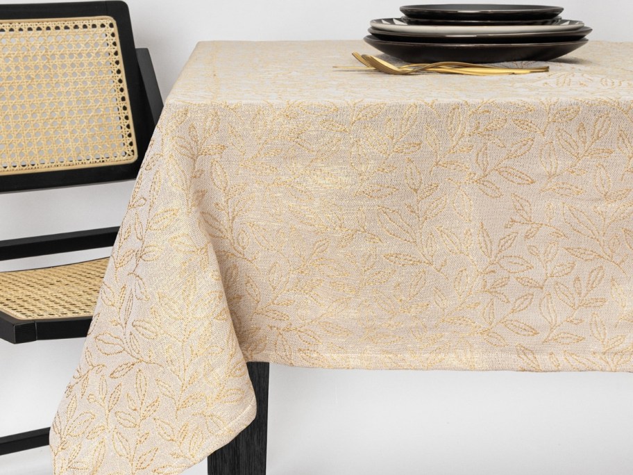 a table with a cream and gold leaf tablecloth next to a chair