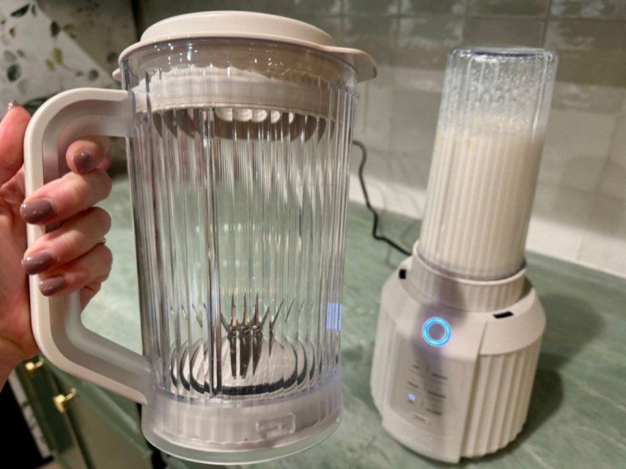 hand holding white blending pitcher next to blender