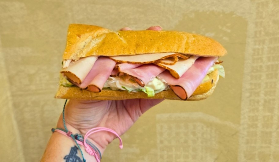 a womans hand holding a 6 inch subway sandwich