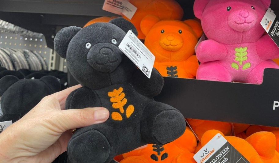 a womans hand holding a black gummy bear skeleton plush