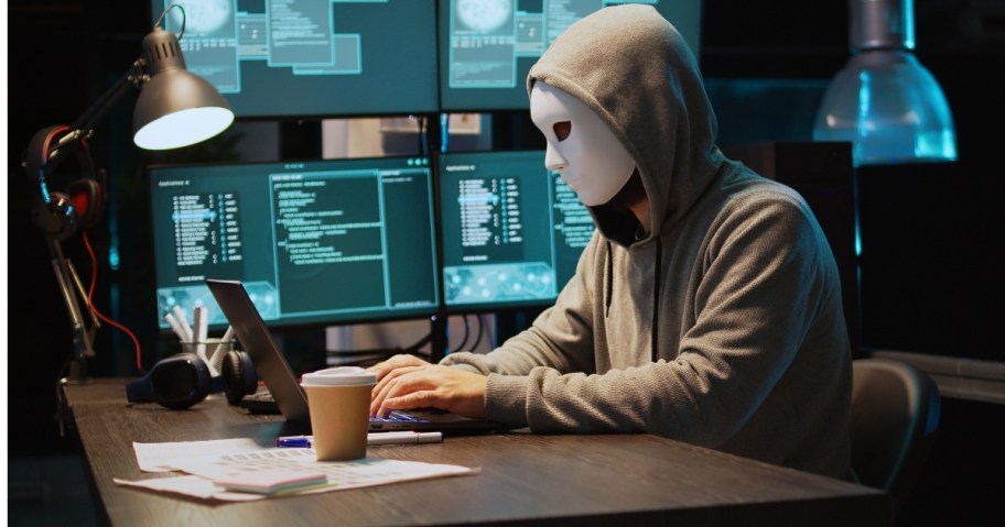 scammer sitting at desk with various scammer screens