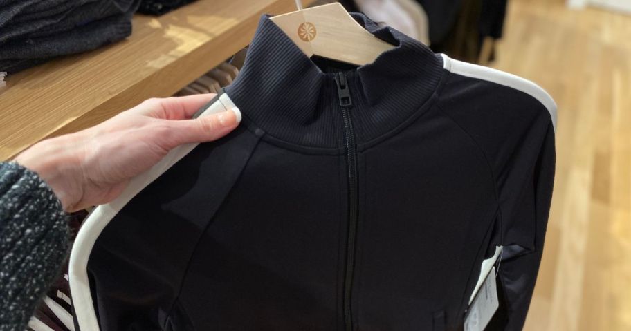 Hand holding a hanger with an Athleta Salutation Jacket on it