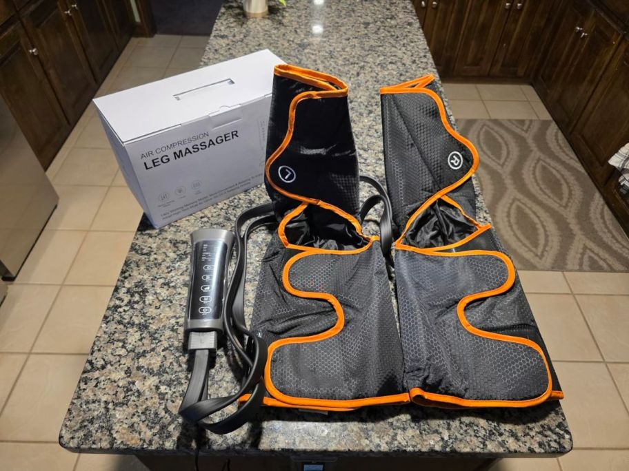 a black and orange leg massager on a kitchen island with its box and remote