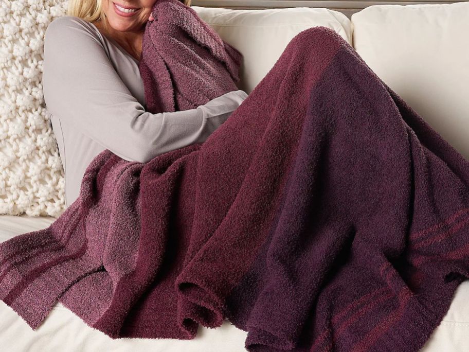 Woman curled up on a couch with a barefoot dreams throw blanket