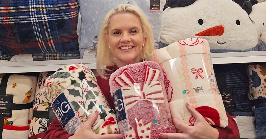 woman holding up 3 christmas print throw blankets in store