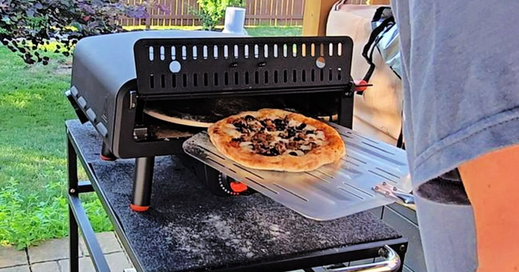 Person removing cooked pizza from Blackstone pizza oven outside on patio