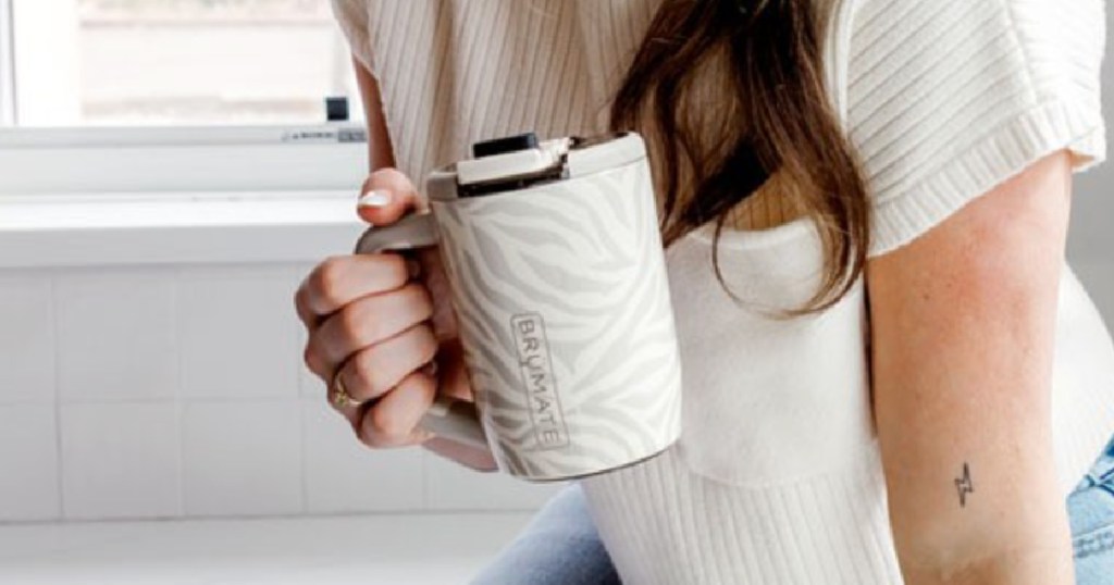 Woman holding roommate, coffee mug, while sitting on kitchen counter