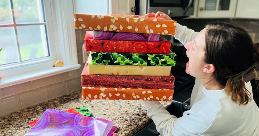 Woman holding stack of boxes wrapped in burger, wrapping paper and taking a bite out of them