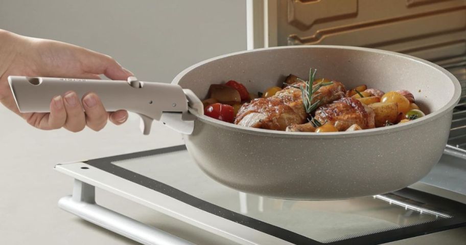Hand holding a Carote Nonstick pan next to an open oven