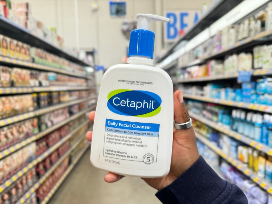 A hand holding up a bottle of Cetaphil facial cleanser.