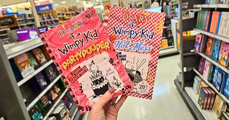 hand holding two Diary of a Wimpy Kid books in a store aisle