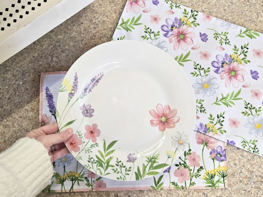 hand holding up a floral print plate with matching placemats in background