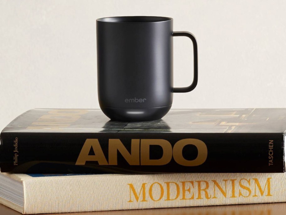 A black Ember coffee mug on a small stack of books.