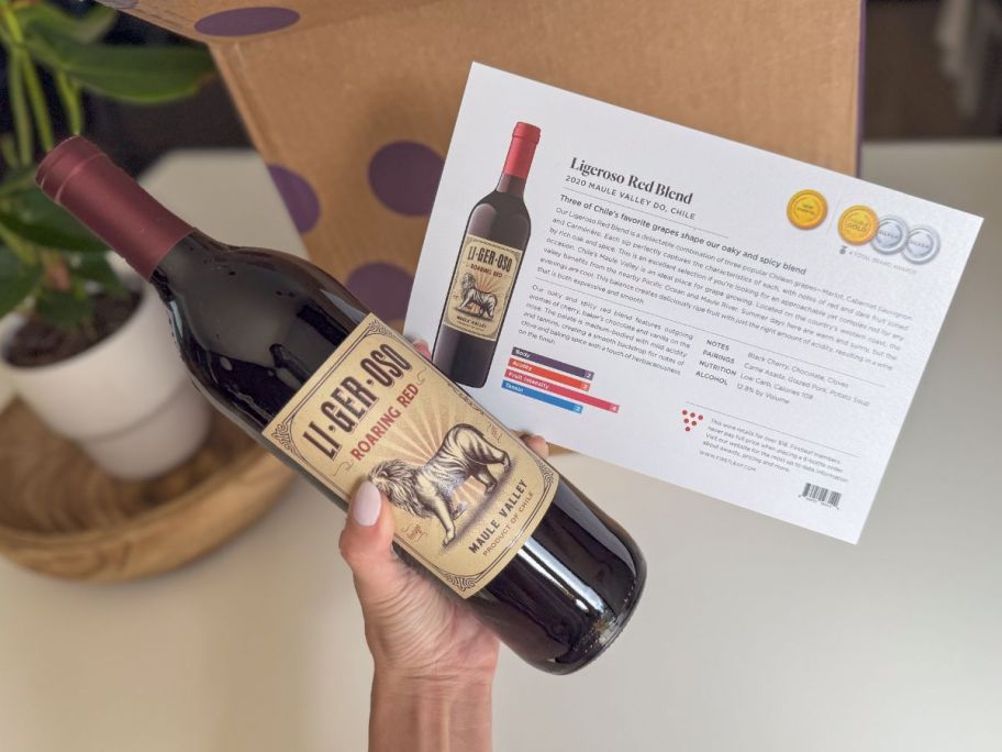 Hand holding a bottle of Firstleaf wine with a card to explain details about the wine