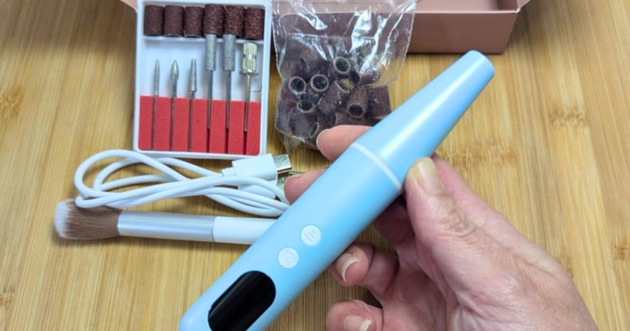 hand holding an electric nail drill, kit with different drill bits behind it