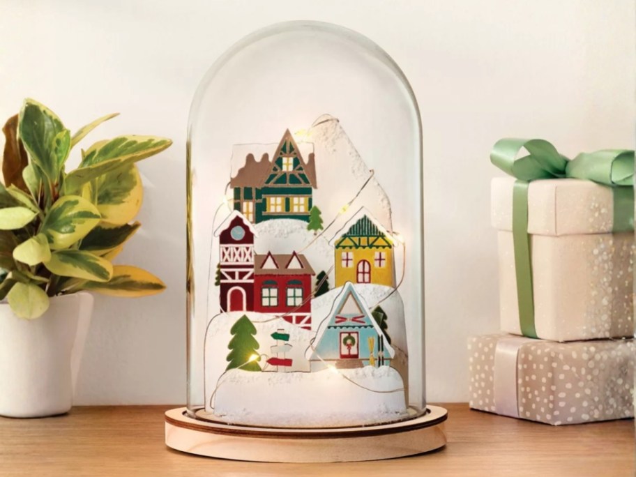 a wooden winter snow village scene in a glass cloche on a table