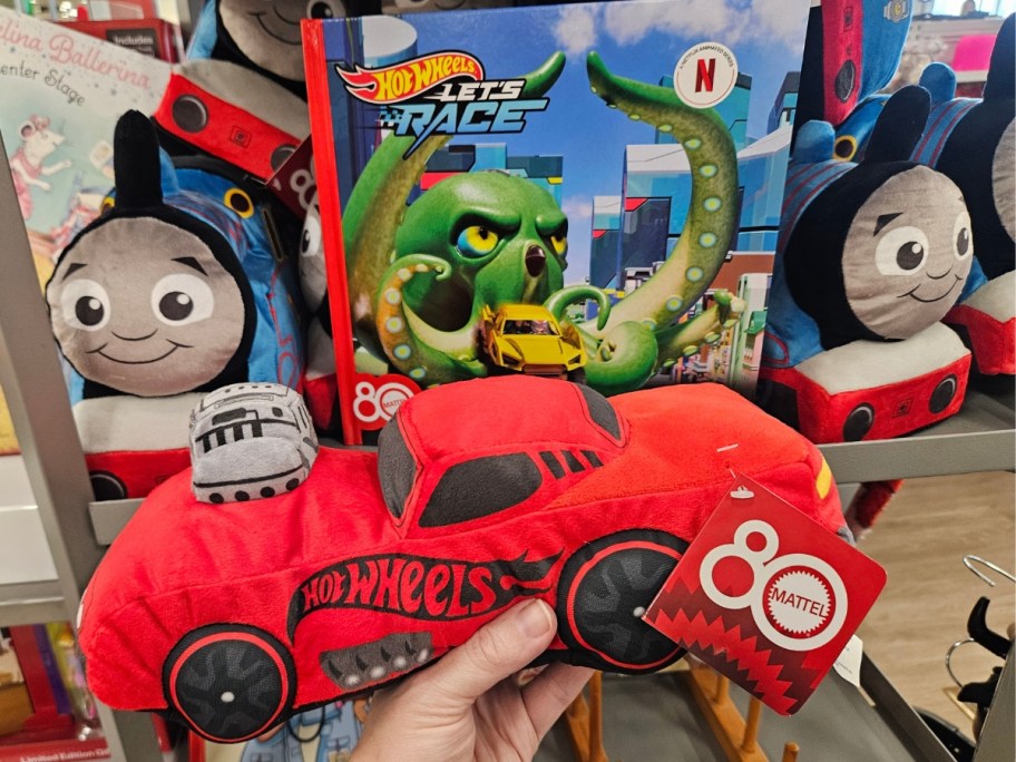 hand holding a plush Hot Wheels car, a Hot Wheels book in the background