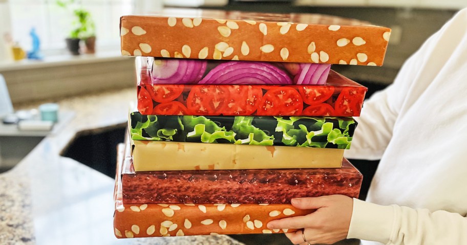 hand holding a stack of boxes wrapped in paper that makes it look like a large hamburger
