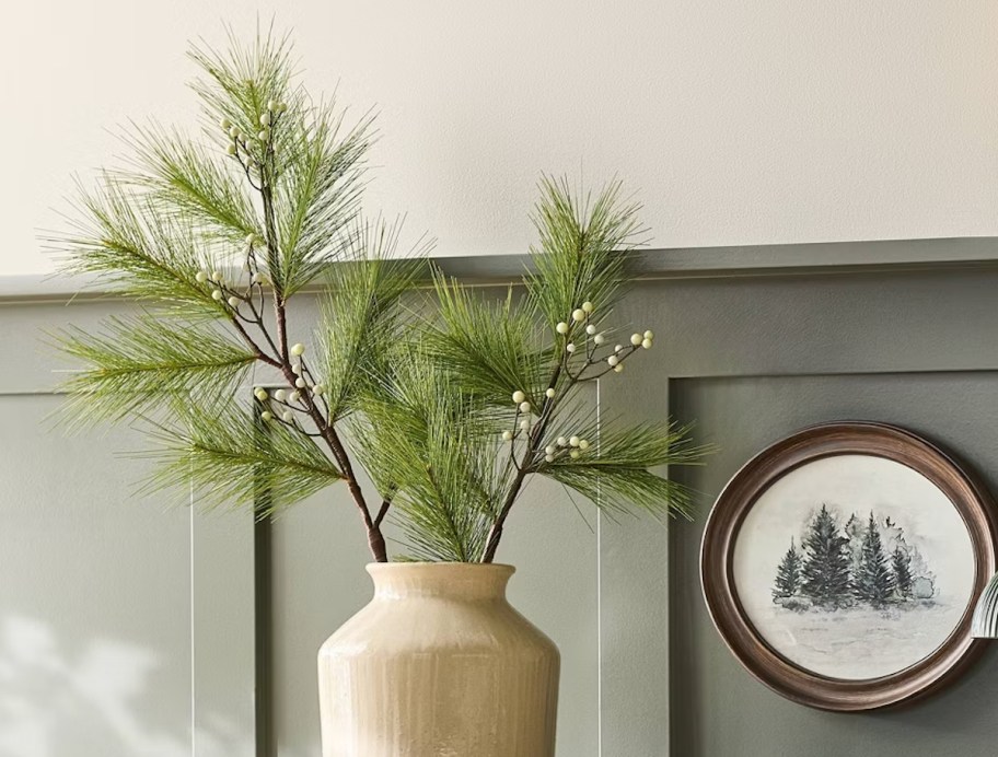 pine stem in beige vase in front of green wall