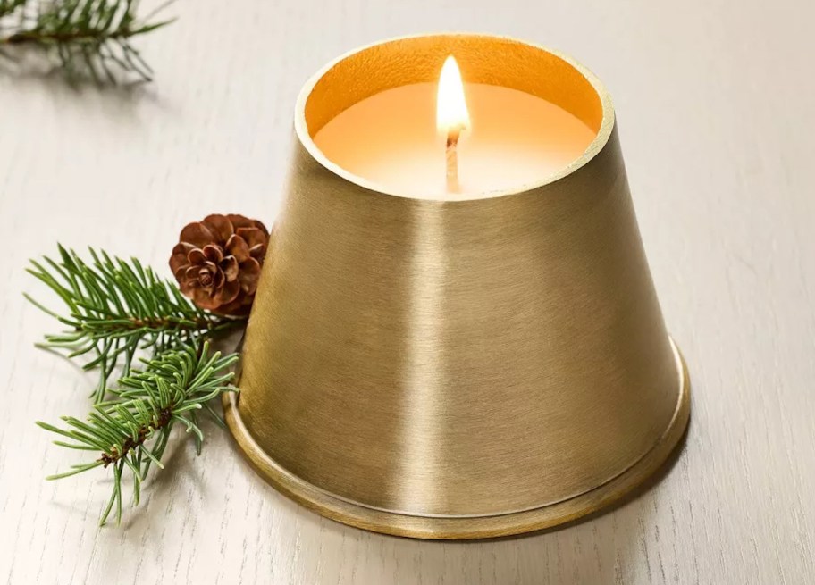 gold bell candle next to greens and pinecone