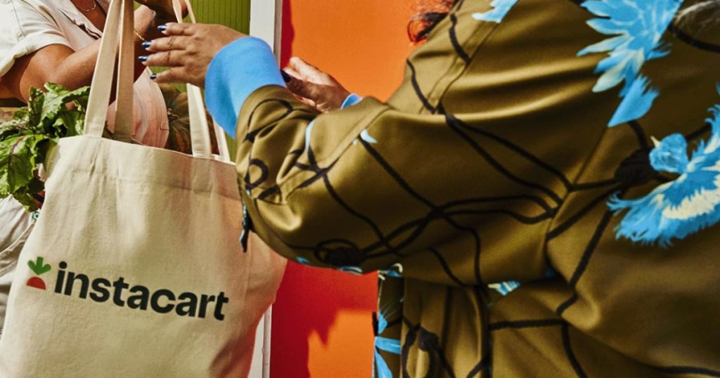 Woman handing another woman an Instacart bag filled with groceries