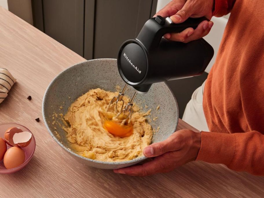 someone beating eggs in bowl with kitchenaid mixer 