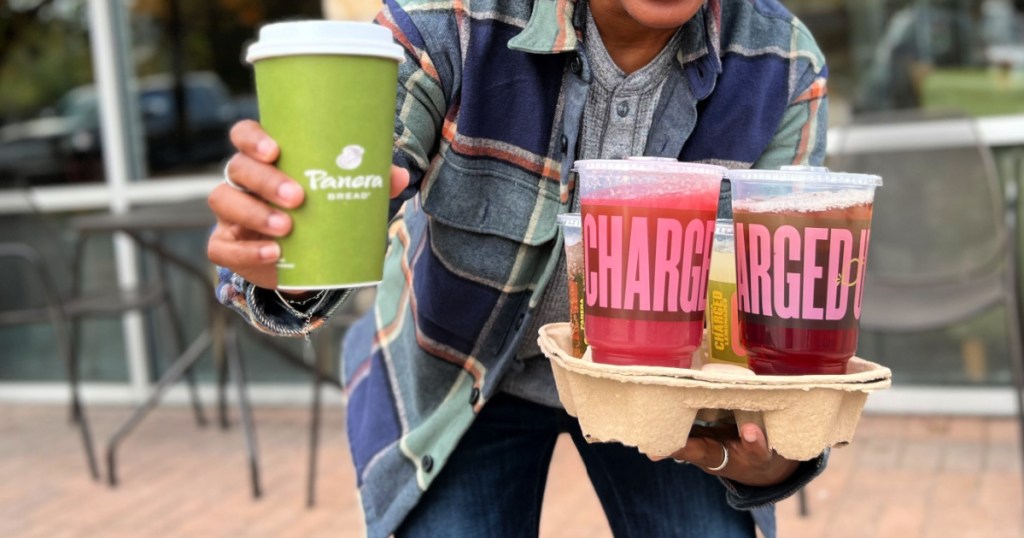 Person holding up several different Panera drinks in drink carrier while standing outside