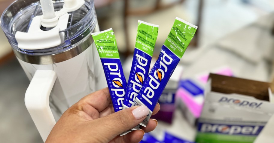 hand holding 3 propel drink mix packets next to a tumbler