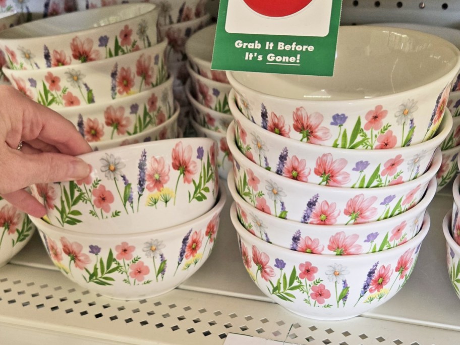 hand grabbing bowl from a stack of floral print bowls on store shelf