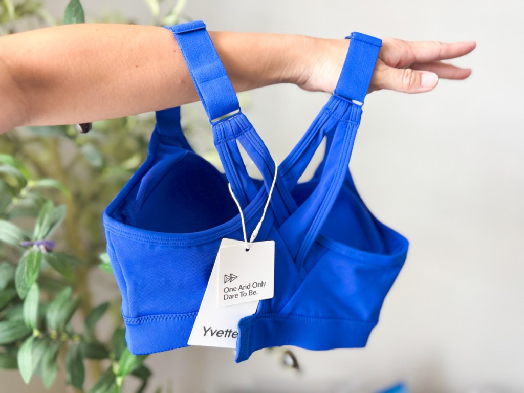 Woman holding up blue Yvette sports bra and showing off the backside