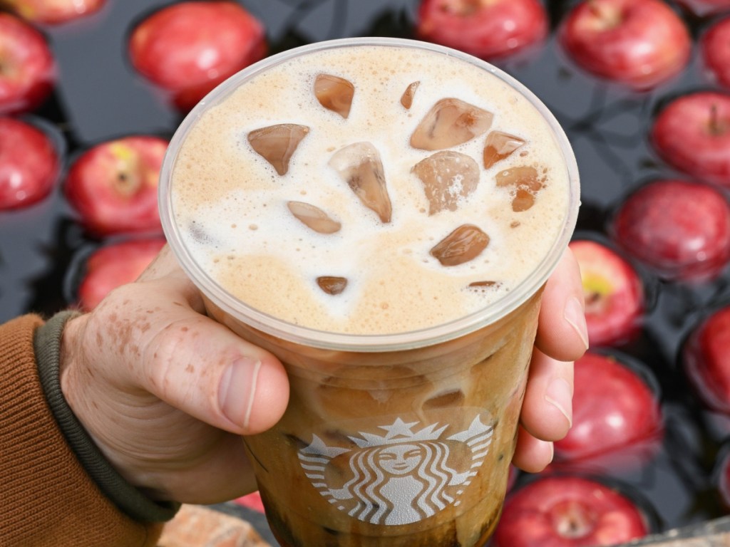 Person holding up iced starbucks drink in front of tub of apples