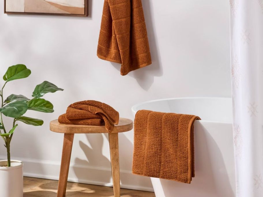 A Bathroom with orange towels hanging on the tub, rack, and stool